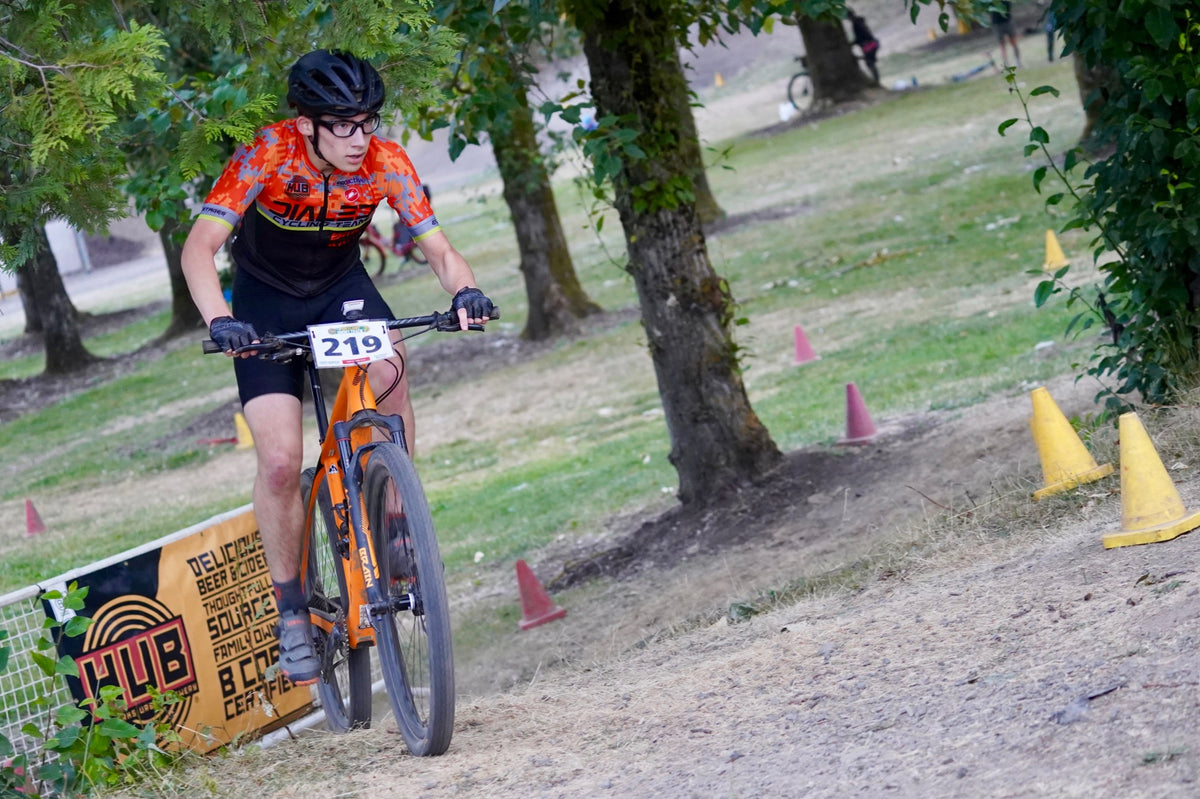 A Dialed Cycling Team junior racing a mountain bike past a sponsor banner