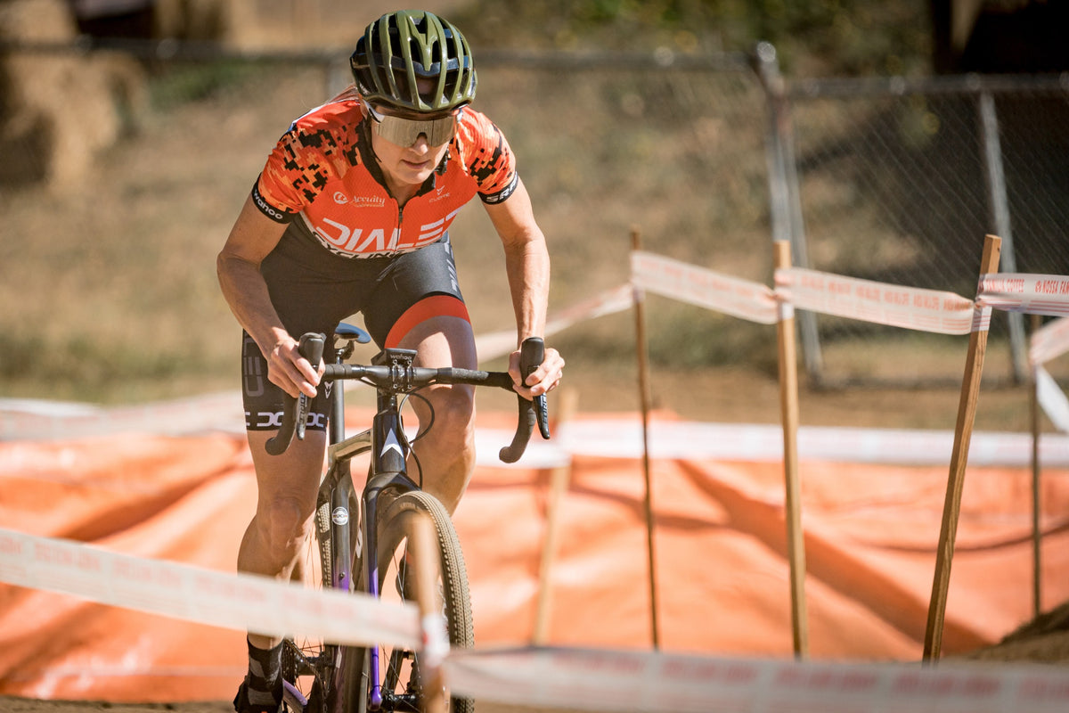 Dialed Cycling Team rider in the orange team kit climbing a cyclocross course