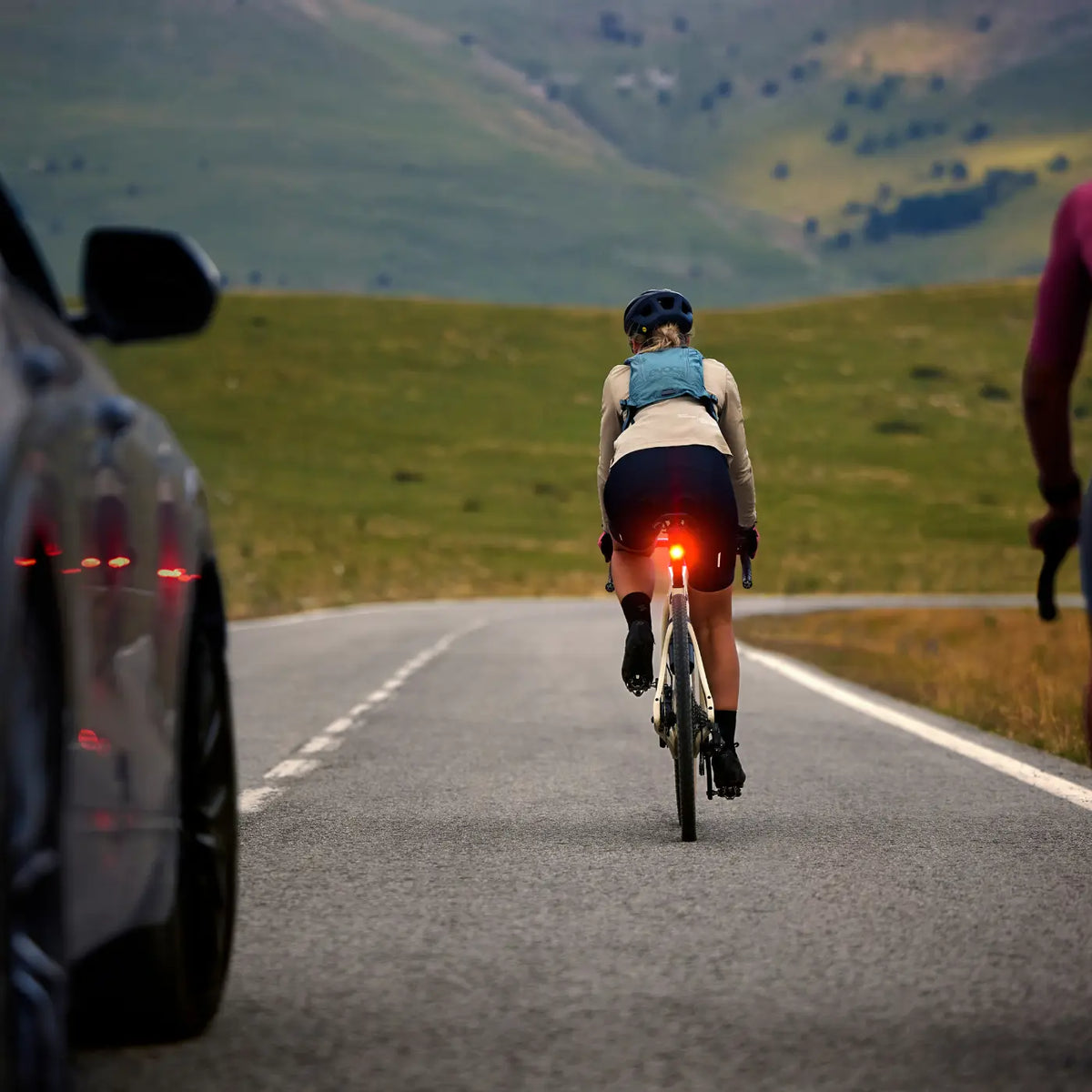 Cyclist riding away from a car with a Garmin Varia rear radar tail light glowing red