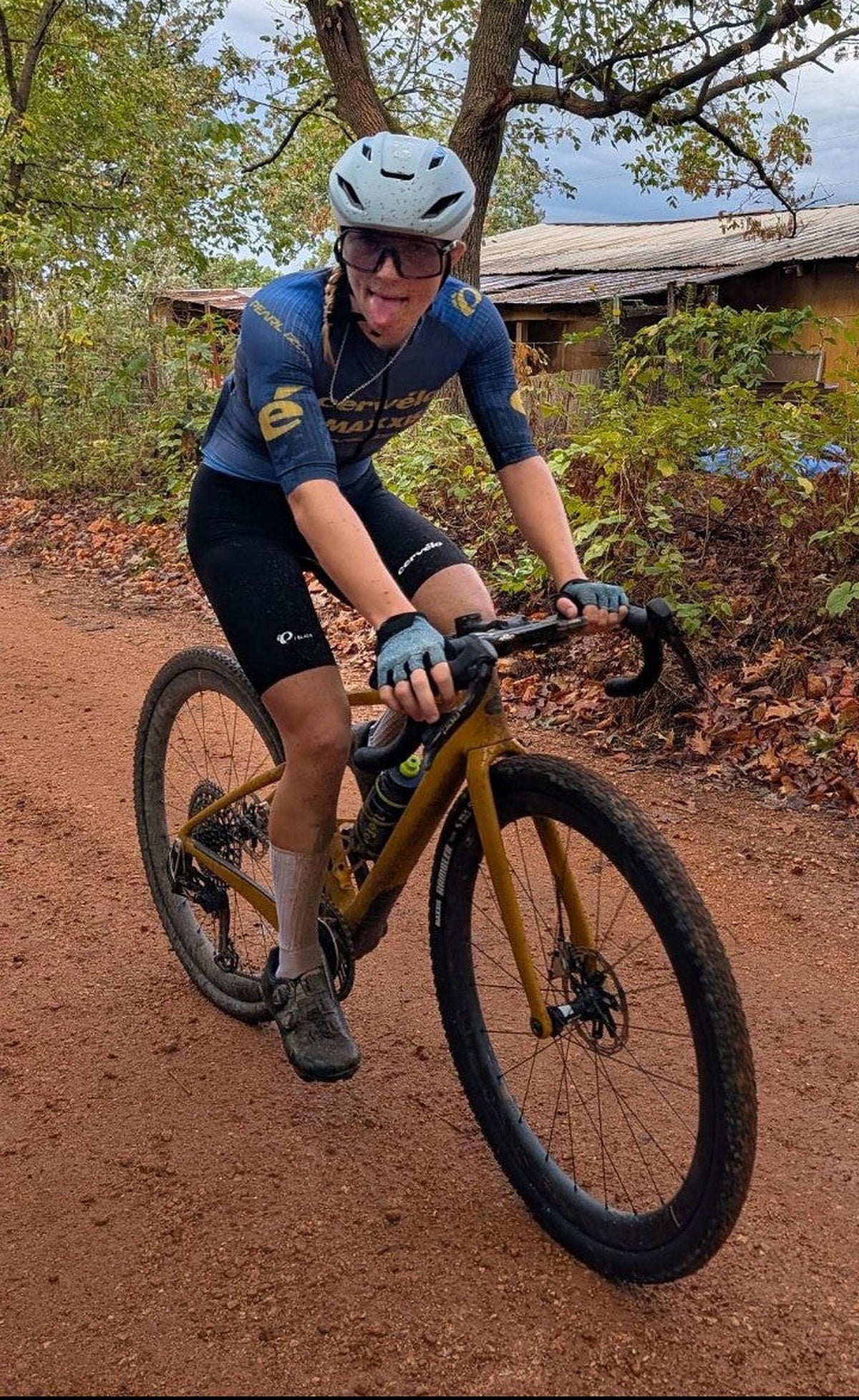 Dialed Cycling Team teammate Kylee Hanel sticks her tongue out for the camera while riding a red dirt road near Bentonville, Arkansas, during Big Sugar weekend