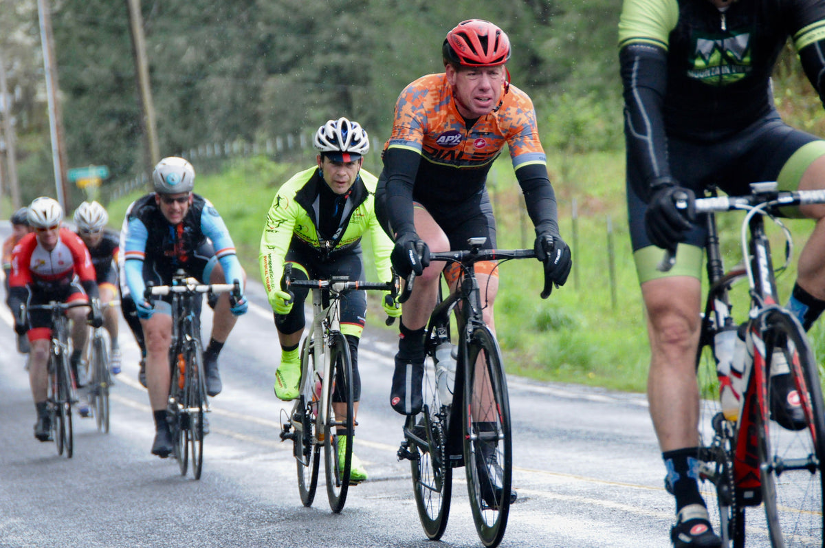 Dialed Cycling Team rider in orange kit leading a group on a wet road