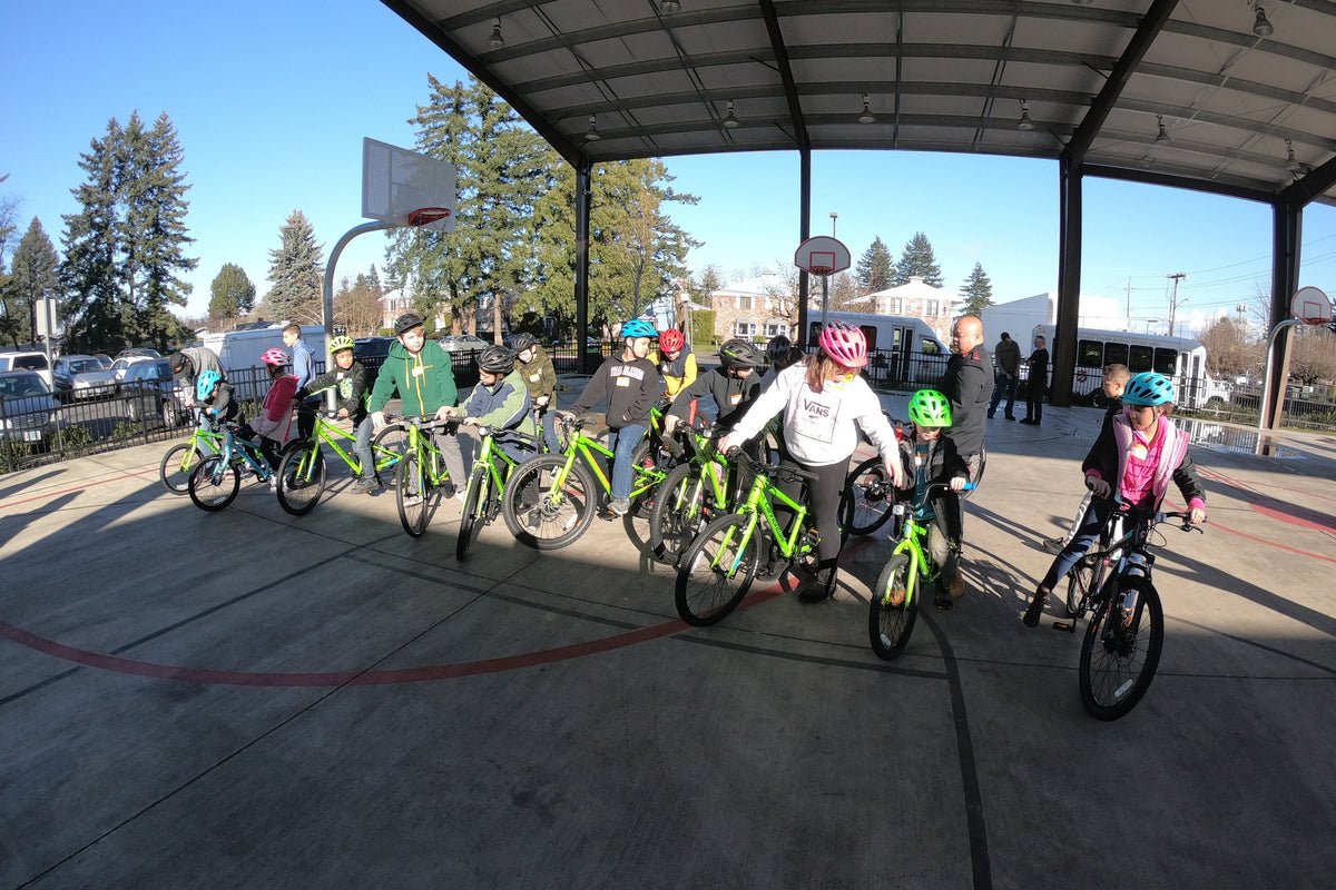 Kids riding new bikes and wearing helmets on a covered school court at a Dialed Cycling Team bike safety event