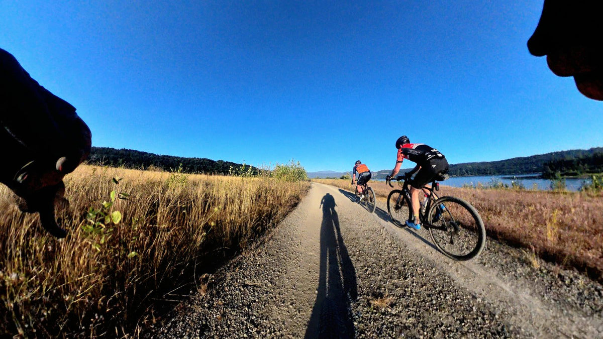 Two Dialed riders on a gravel path by a lake