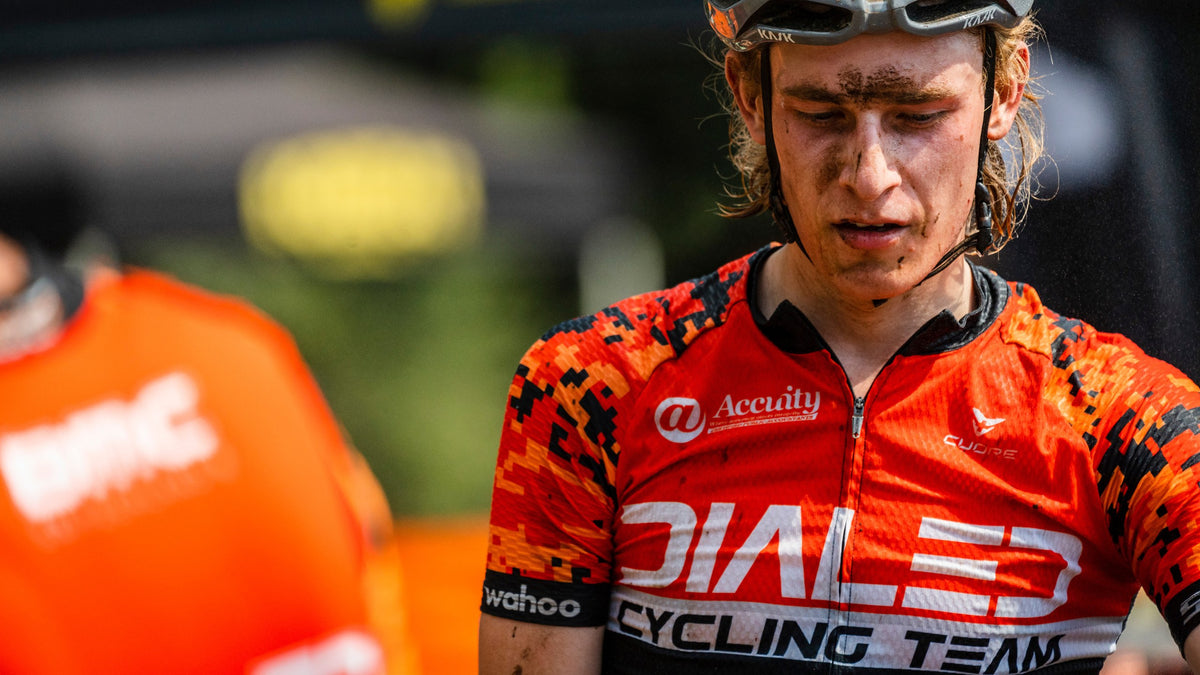 A mud-splattered Dialed Cycling Team junior in the orange team jersey after a mountain bike race